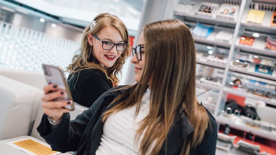 Zwei junge Frauen kommunizieren in der Universitätsbibliothek mit Handys